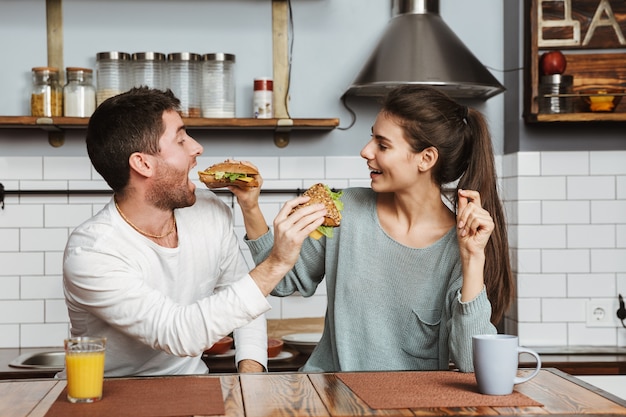 自宅で朝食時にキッチンに座って、サンドイッチでお互いを養う若いカップル