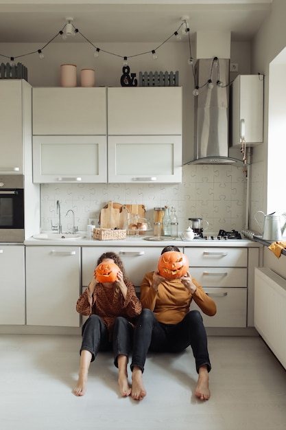 Молодая пара сидит на полу кухни и держит тыквы на Хэллоуин