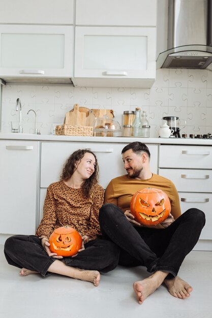 Giovani coppie che si siedono sul pavimento della cucina e che tengono le zucche di halloween