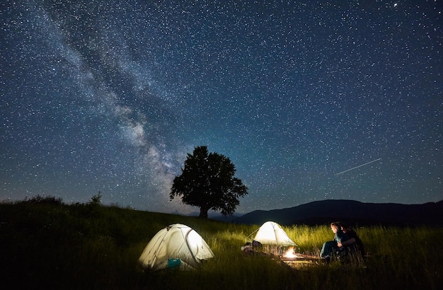 美しい夜空の下でキャンプファイヤーのそばに座っている若いカップル