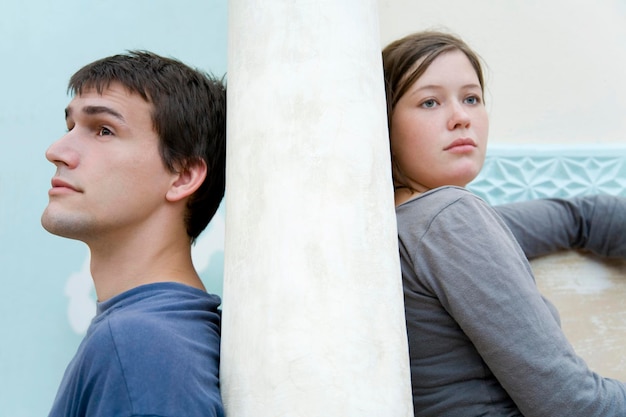 Photo young couple sitting on opposites sides of a stone wall