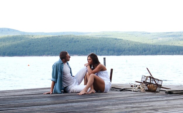 Photo young couple sitting on pier against lake