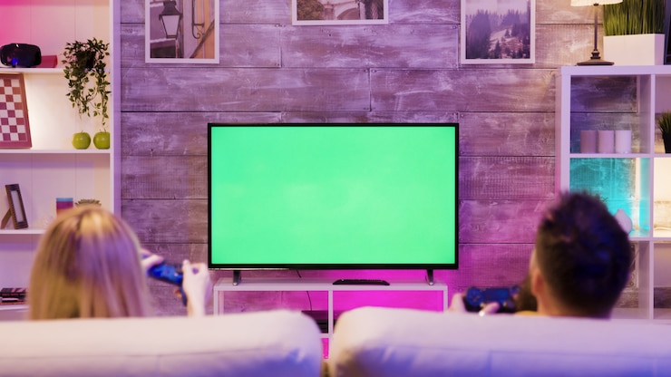 Photo ソファに座って、緑色の画面でテレビでオンラインゲームをプレイしている若いカップル。幸せな関係。ゲーマーのカップル。