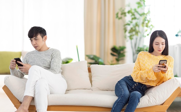 Young couple sitting on sofa using smartphone and ignoring each other