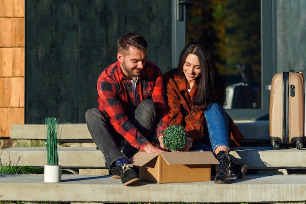 Young couple sitting on stairs having fun unpacking boxes after moving to new house.