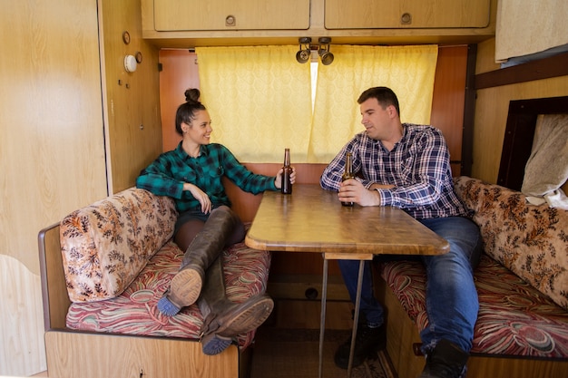 Young couple sitting at table in campervan talking about something. Drink beer