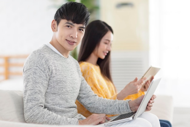 Young couple sitting and using laptop and tablet together in the living room