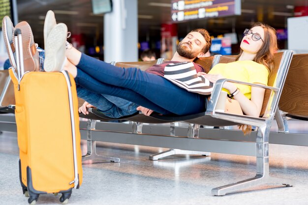 공항 대기실의 의자에서 자는 젊은 부부. 비행기를 오래 기다리다