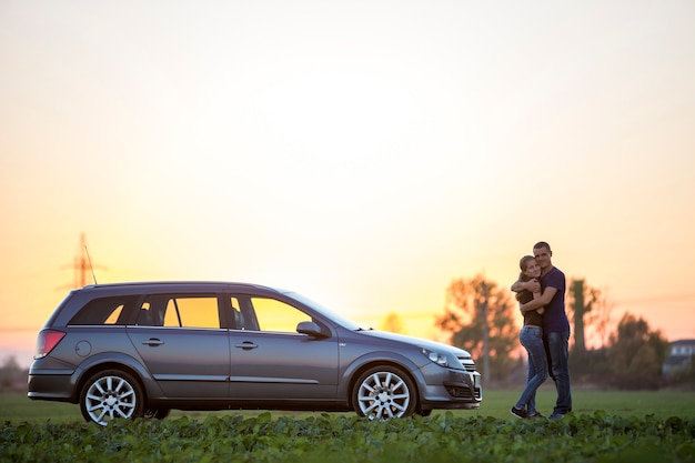 young couple, slim attractive woman with long ponytail and handsome man standing at silver car