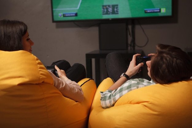 Молодая пара улыбается друг другу, держа геймпады, вместе играя в видеоигры