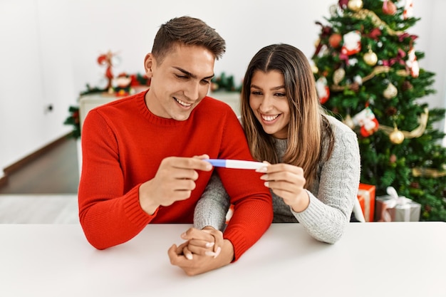 Young couple smiling happy holding pregnancy test. Sitting on the table at home.