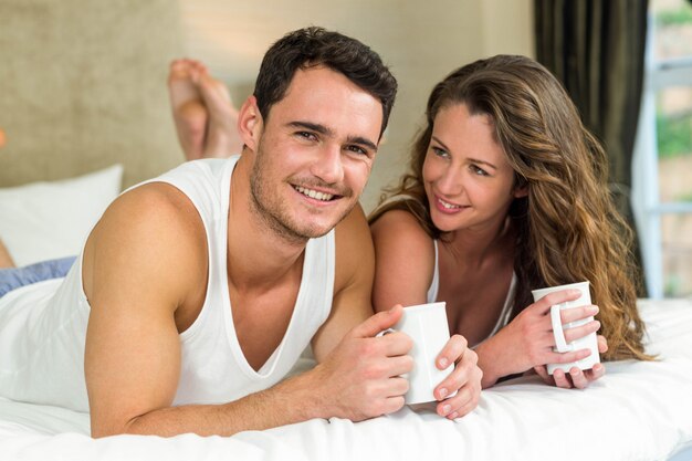 Young couple smiling and having cup of coffee on bed