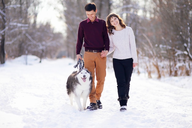 Young couple smiling and having fun in winter park with their husky dog.