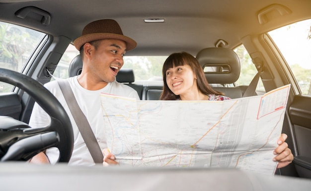 Foto giovani coppie che sorridono facendo uso di una mappa durante un viaggio per le direzioni che si siedono in un'automobile