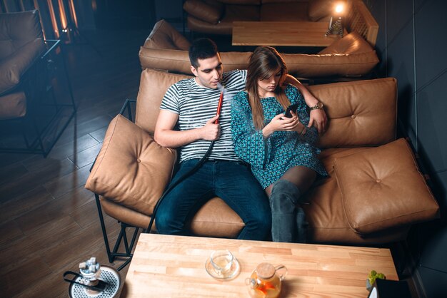 Young couple smoking hookah on leather couch