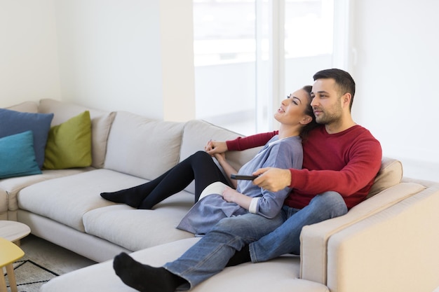Молодая пара на диване вместе смотрит телевизор в своем роскошном доме