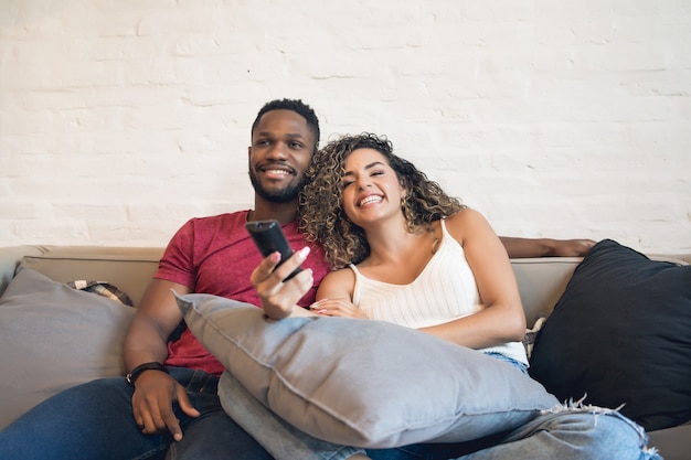 Young couple spending time together and watching tv series or movies while sitting on couch at home.