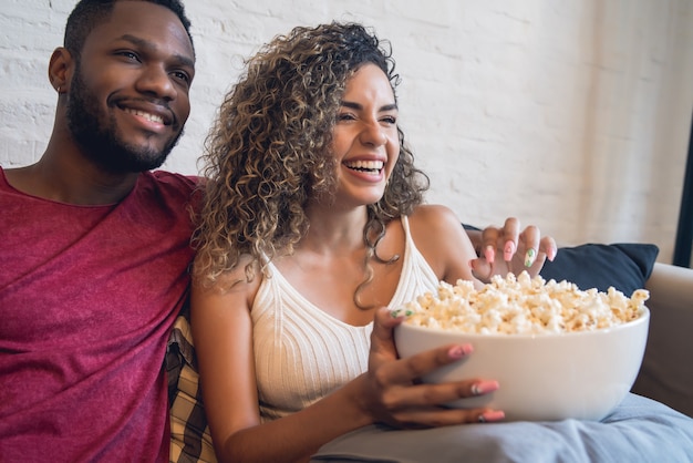 Young couple spending time together and watching tv series or movies while sitting on couch at home.