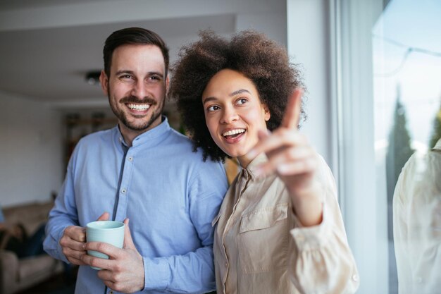 Young couple standing by the window Woman pointing at something