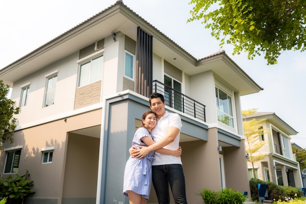 young couple standing and hugging together looking happy in front of their new house