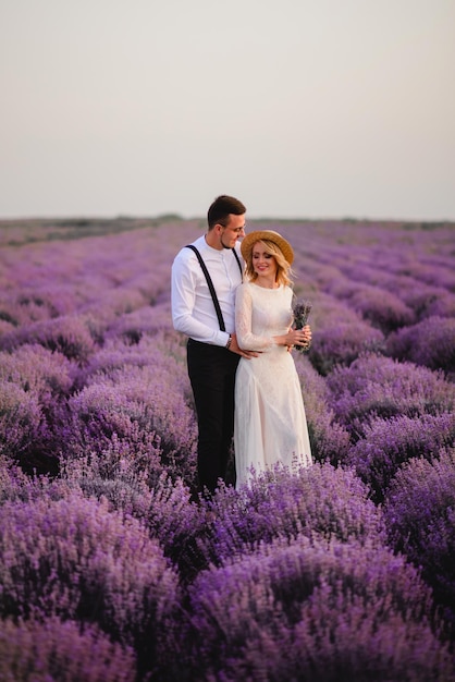 Young couple standing in middle of blooming lavender field at sunrise