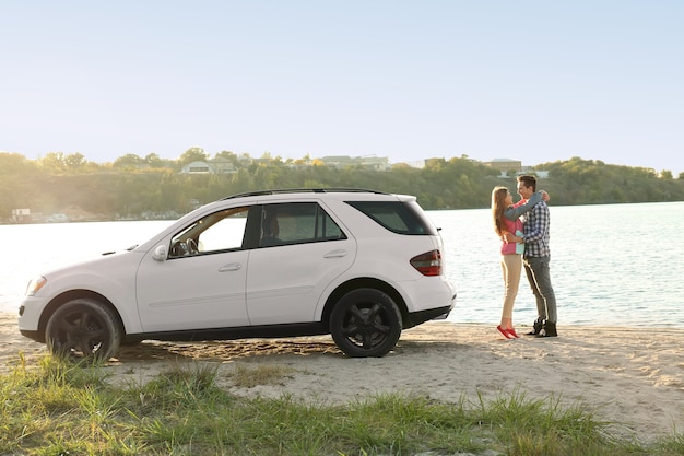 Young couple standing near car on river bank