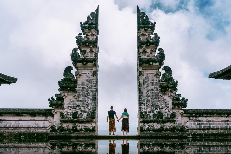 若いカップルが寺院の門に立って、インドネシアのバリ島のレンプヤンルフル寺院でお互いの手を繋いでいます。ヴィンテージトーン。