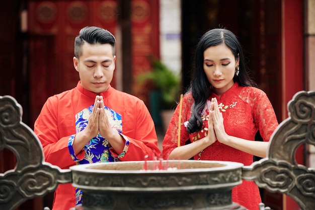 Foto coppia giovane in piedi con gli occhi chiusi e tenendosi per mano in gesto di preghiera quando si trova in un'antica urna di bronzo con bastoncini di incenso