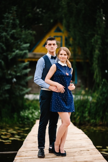 The young couple standing on a wooden bridge above the lake on the background a old house on an island