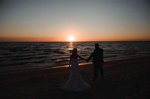 Young couple stands at the sea beach looking at sunset.