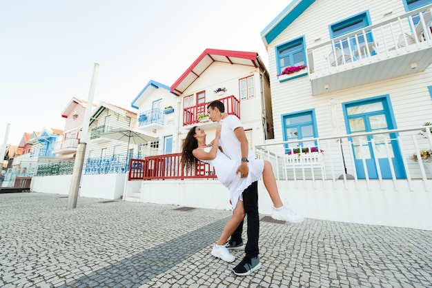 Молодая пара остается в позе танго и смотрит друг на друга в Авейру, Португалия, возле ярких и мирных домов.