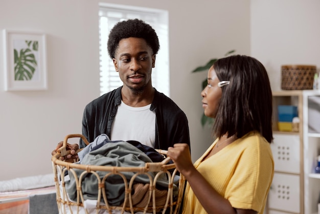 A young couple of students live together in an apartment the\
woman is doing household chores sorting laundry in a wicker basket\
the man is helping the girl to put in the washing machine