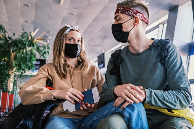 Young couple of stylish tourists sit at the airport with passports in their hands caucasian man and