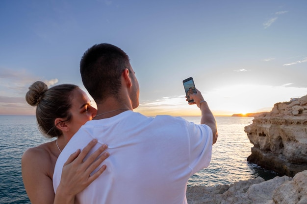 Foto una giovane coppia di sunset selfie sulla spiaggia un colpo orizzontale ravvicinato da dietro catturando l'uomo ph