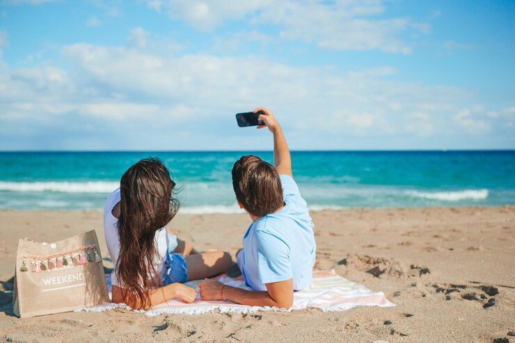 Photo ビーチでスマートフォンでセルフィーを撮っている若いカップル