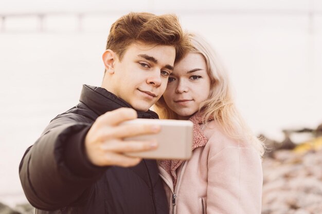 写真 若いカップルが海と空の向こうに立ってスマートフォンでセルフィーを撮っている