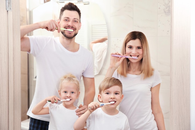 Young couple and their children brushing teeth in bathroom