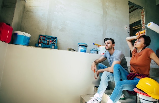 Young couple tired during the renovation of a new house and resting while sitting on the stairs