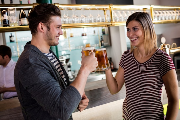 Giovani coppie che tostano la tazza di birra dal contatore