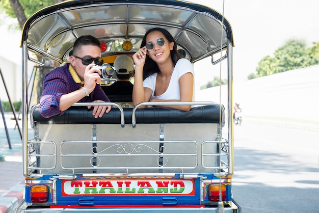 Young couple tourists traveling on local Tuk Tuk taxi in Bangkok, Thailand 