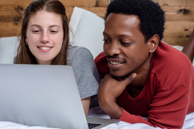 Giovani coppie che utilizzano computer portatile in un letto a casa.