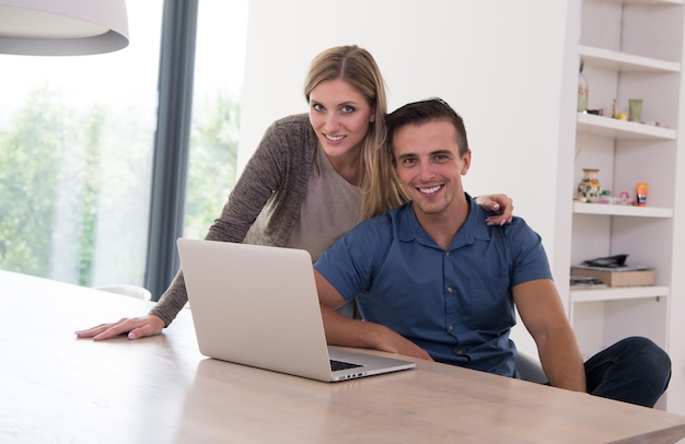 Young couple using laptop computer at luxury home together, looking at screen, smiling.