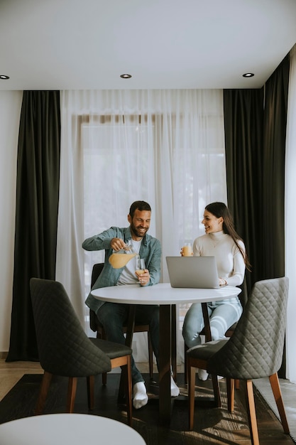 Young couple using laptop computer on the table in the living room and drinking orange juice