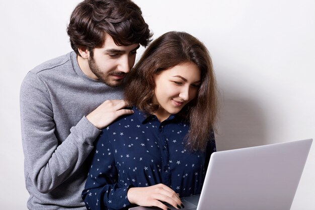 Foto giovani coppie che per mezzo insieme del computer portatile. l'uomo barbuto attraente si è vestito nella tenuta casuale del maglione