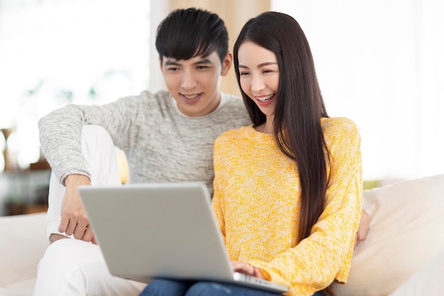 Молодая пара использует ноутбук и вместе смотрит видео в гостиной