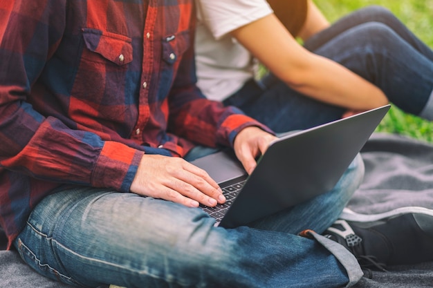 A young couple using and looking at laptop computer while sitting in the park together