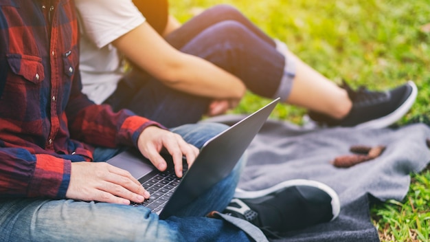 A young couple using and looking at laptop computer while sitting in the park together