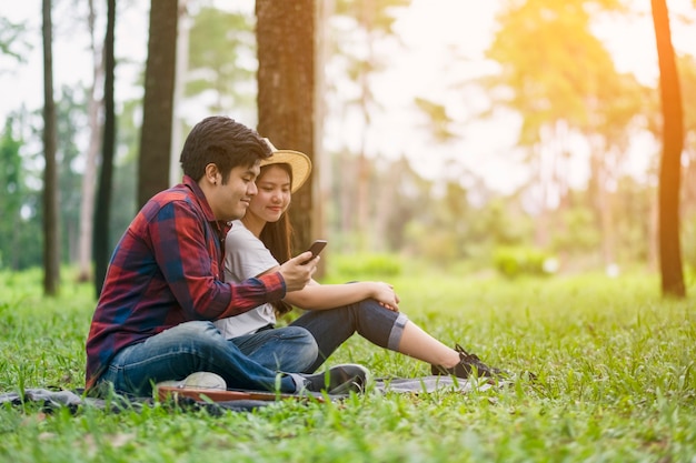 A young couple using and looking at mobile phone while sitting in the park together