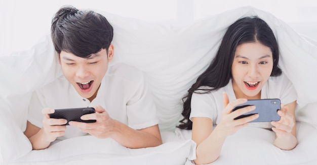 Young couple using phone in bed with cheerful expressions