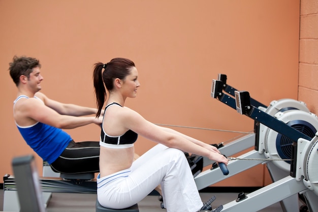 Photo young couple using a rower in a sport centre